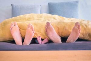 Photo showing three pairs of feet under a blanket: a couple and a baby. The story is about postpartum sex.