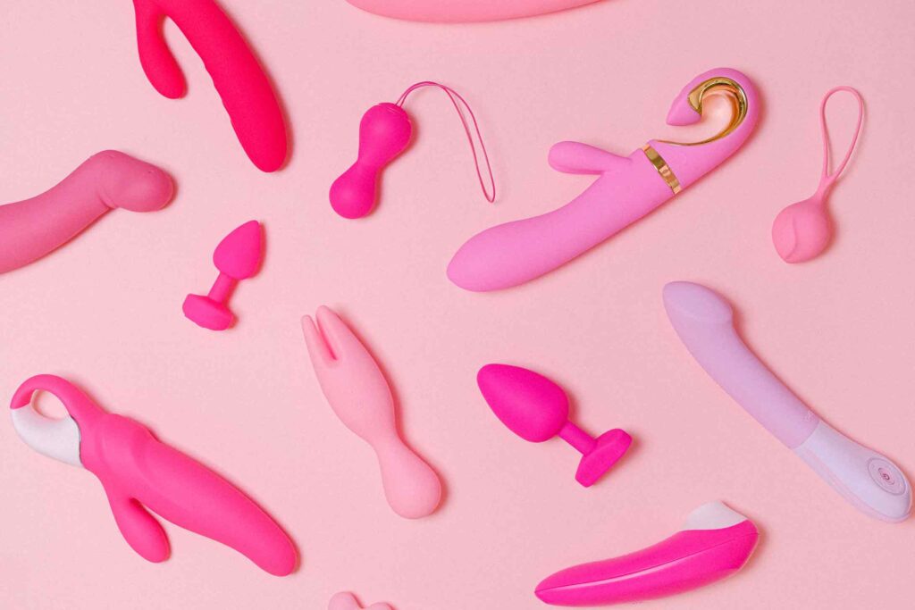 Photo of many sex toys on a pink background including g-spot vibrators, yoni eggs and plugs