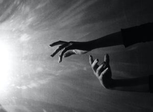 Black and white photo of two hands in the water reaching up to portray us reaching for our higher self and using shadow work to rediscover our selves.