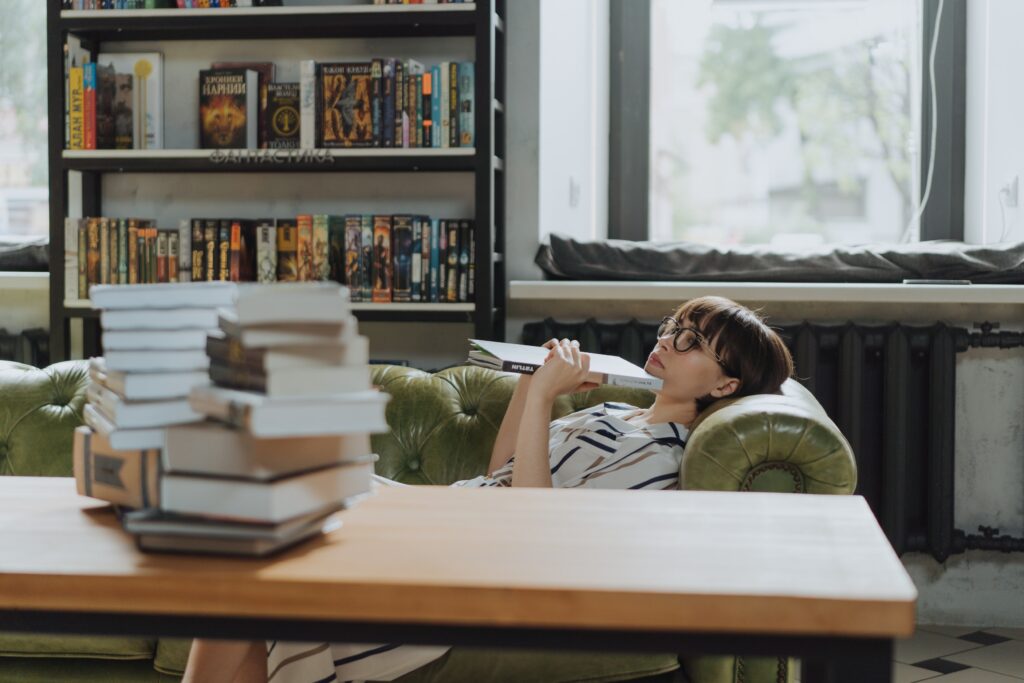 Photo of a woman lying on a couch with a book, staring into nothing, obviously comtemplating something. This is to display how intelligent people can often become trapped in their minds and neglect their bodies and physical needs.