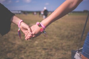Photo of two holding hands with pink bands, could be women, to depict an emotional connection for an article by Lisa Opel from pleasepinchmehard about navigating emotional connections to more than one person