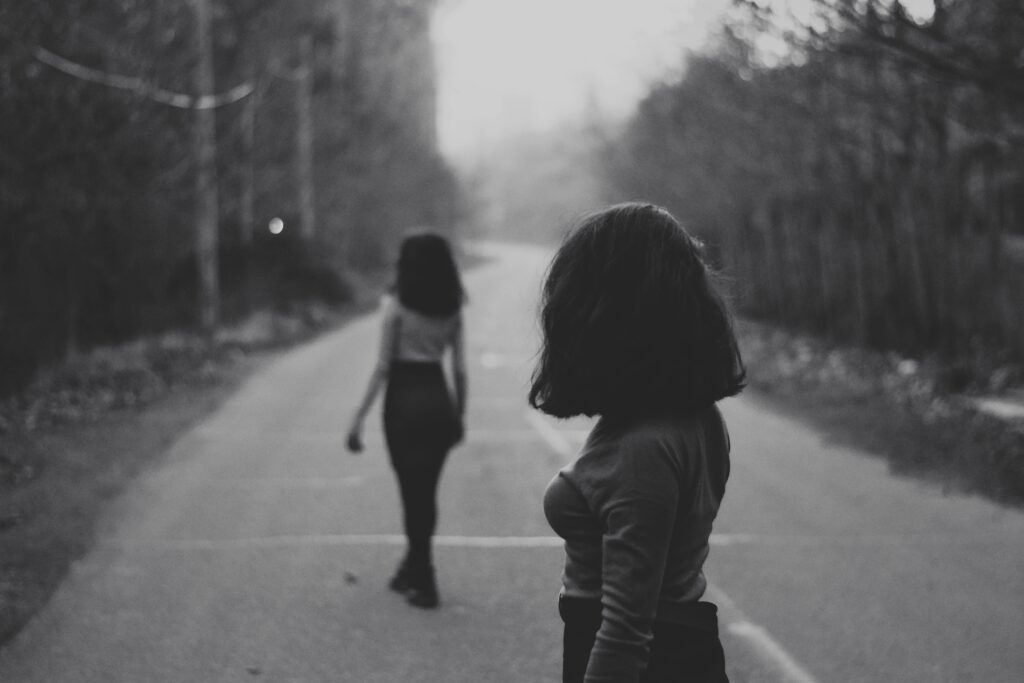 Black and white photo of two women, one walking away and the other watching here to depict jealousy truths covered in an article by Lisa Opel for pleasepinchmehard