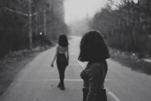 Black and white photo of two women, one walking away and the other watching here to depict jealousy truths covered in an article by Lisa Opel for pleasepinchmehard