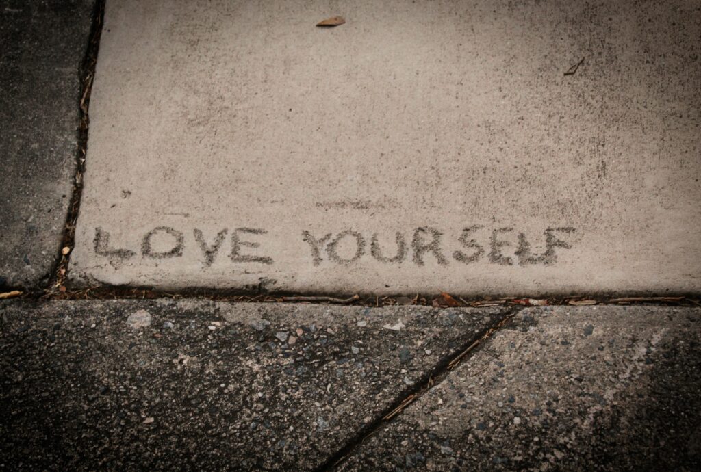 Photo of the words "Love yourself" etched into the pavement to underline the essence of the article by Lisa Opel for pleasepinchmehard about the interplay between weight, libido and self-image