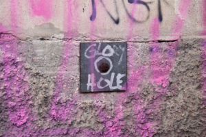 Photo of a hole in the wall with the writing glory hole around it with pink graffiti as it could be at a kinky party