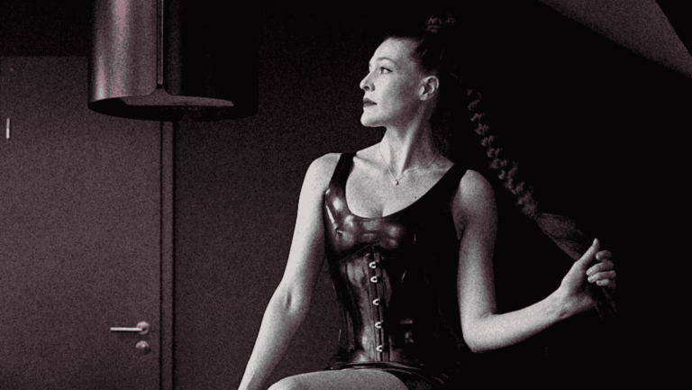 Woman in black latex holding long braid, exuding dominant energy with powerful side gaze