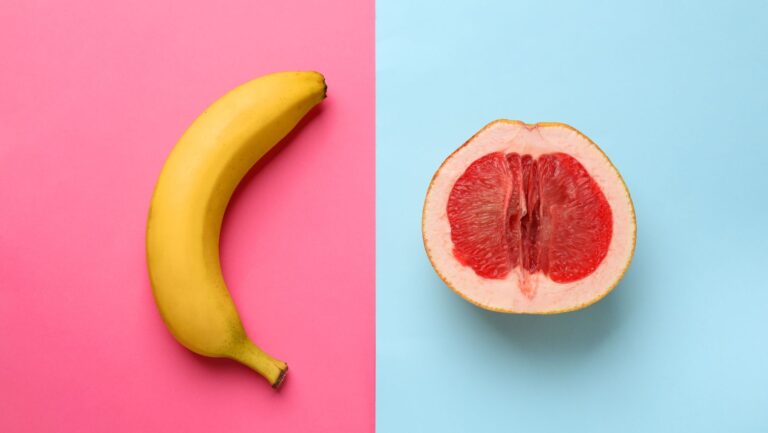 Banane und halbierte Grapefruit als Symbolbild für Penis und Vulva auf pinkem und blauem Hintergrund