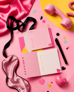 KI-generiertes Stillleben mit pinken Karten, Satin, Telefon, Schleife und Checklisten als Symbol für spielerische Lust-Erkundung, Fantasien und Konsens.